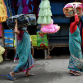 Two women are carrying garments items on their heads for selling at a market in Howrah, India