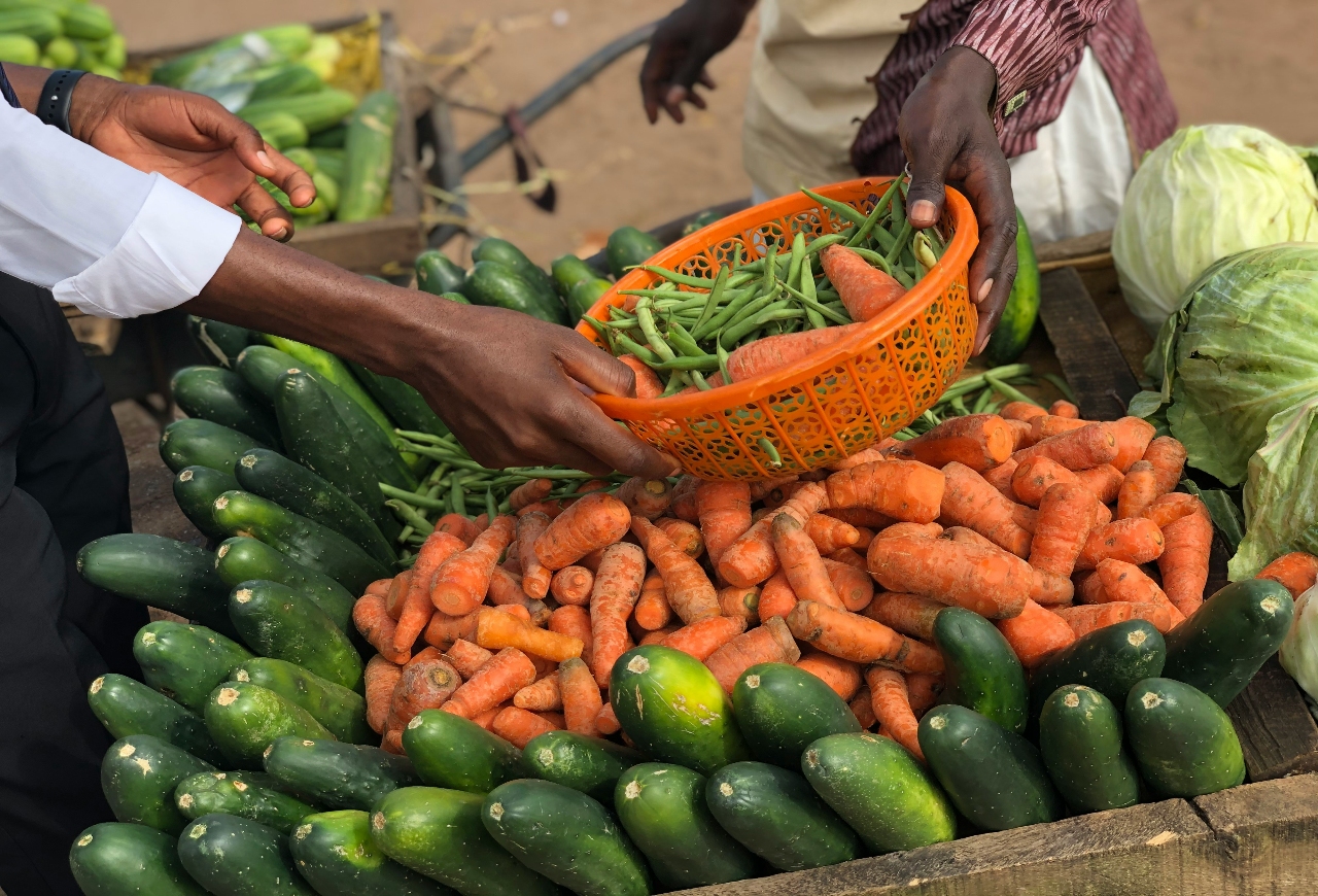 person in white long sleeve shirt holding green cucumber in a roadside market in Nigeria